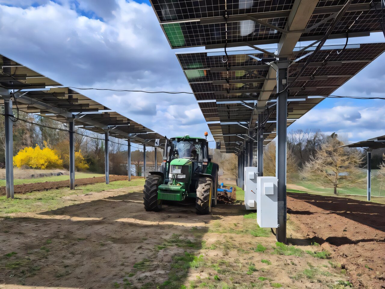 Tractor bajo paneles solares agrofotovoltaicos sobre un terreno agrícola con huellas de maquinaria