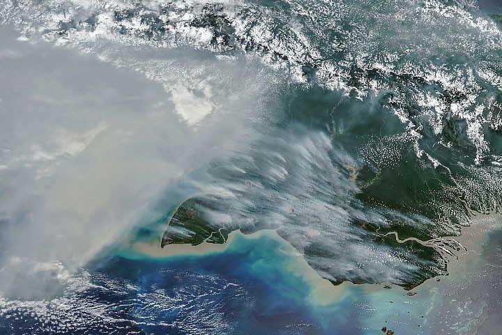 Imagen satelital de humo sobre el tercio sur de Nueva Guinea, con nubes y cordilleras visibles al norte.