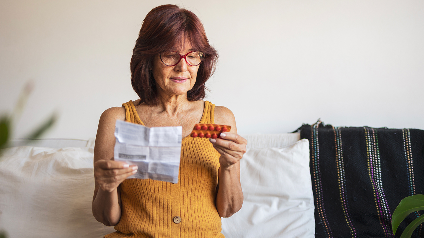 Una mujer mayor lee el prospecto de una terapia hormonal, imagen usada para ilustrar un estudio sobre estrógenos y marcadores cerebrales de Alzheimer